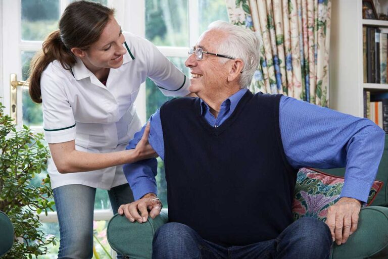 Two older adults and a staff member sharing a light conversation in a sunny common room.